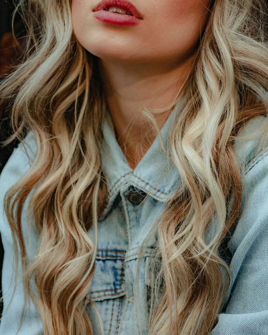 Detalle de ondas largas con mechas rubias sobre una camisa vaquera.